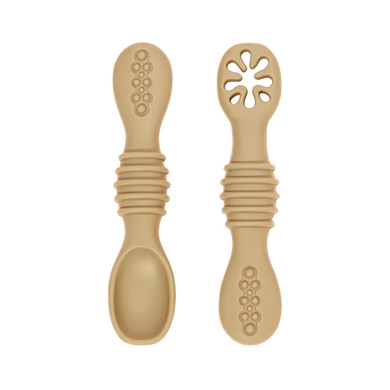 Two beige silicone baby training spoons, one solid and one with a flower-shaped opening, featuring textured handles.