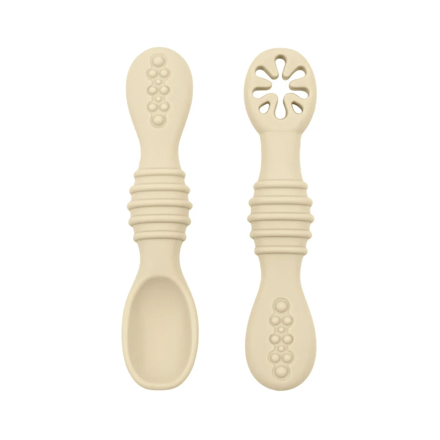 Two beige silicone baby training spoons, one solid and one with a flower-shaped opening, featuring textured handles.