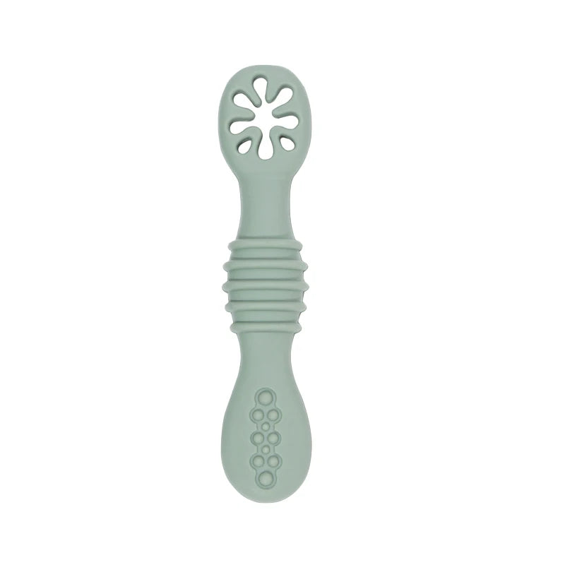 Soft sage green silicone baby training spoon with textured handle and flower-shaped feeder.