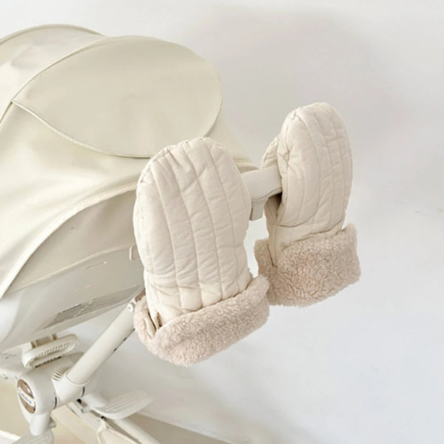 Quilted cream stroller mittens with plush fleece lining attached to a light-colored stroller handle.