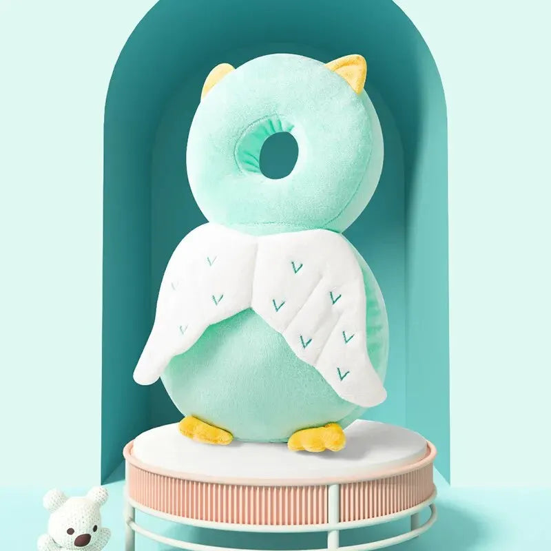 Mint green baby head protection pillow with white angel wings and yellow accents.
