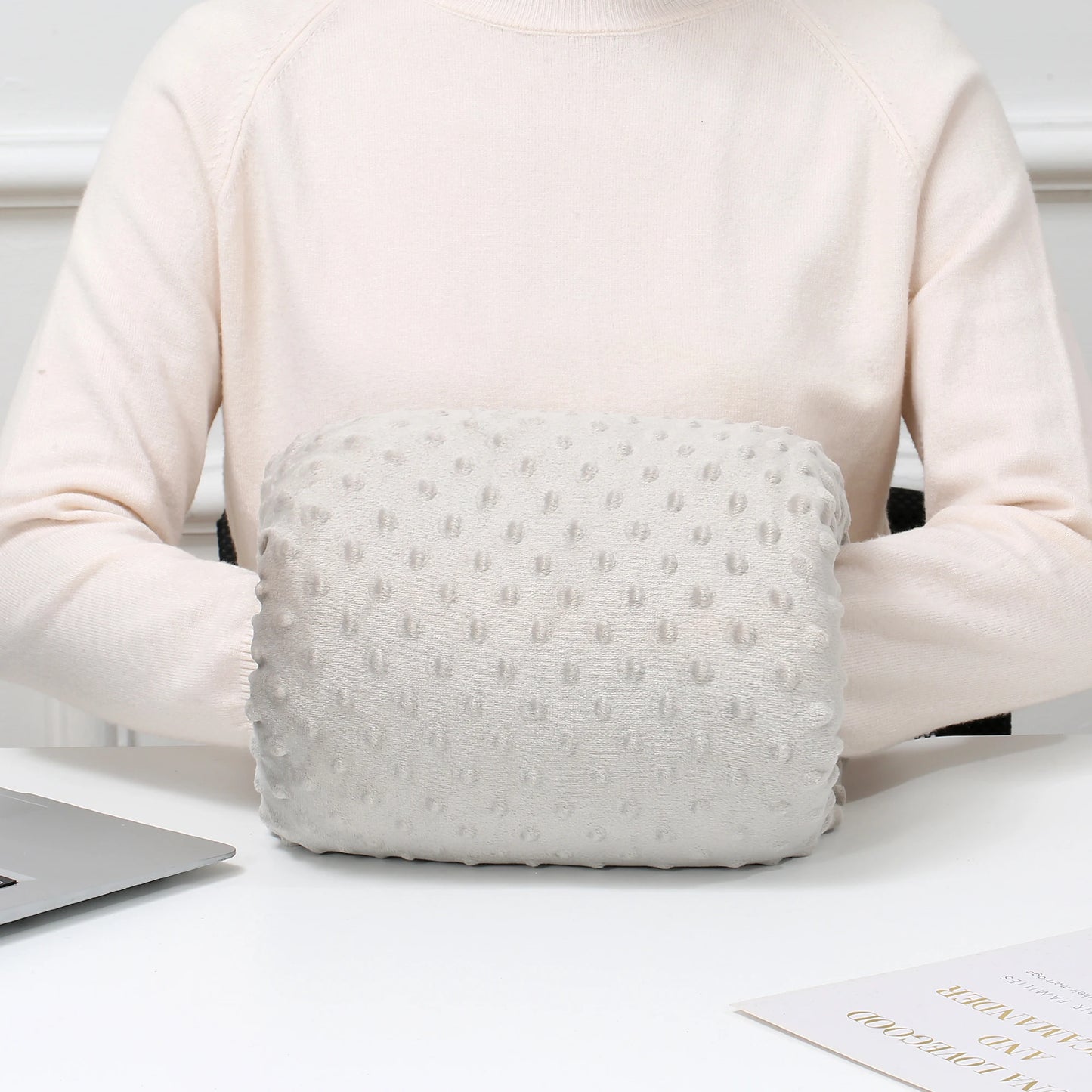 Light gray ergonomic nursing arm pillow with textured dots, worn by a person in a cream sweater.