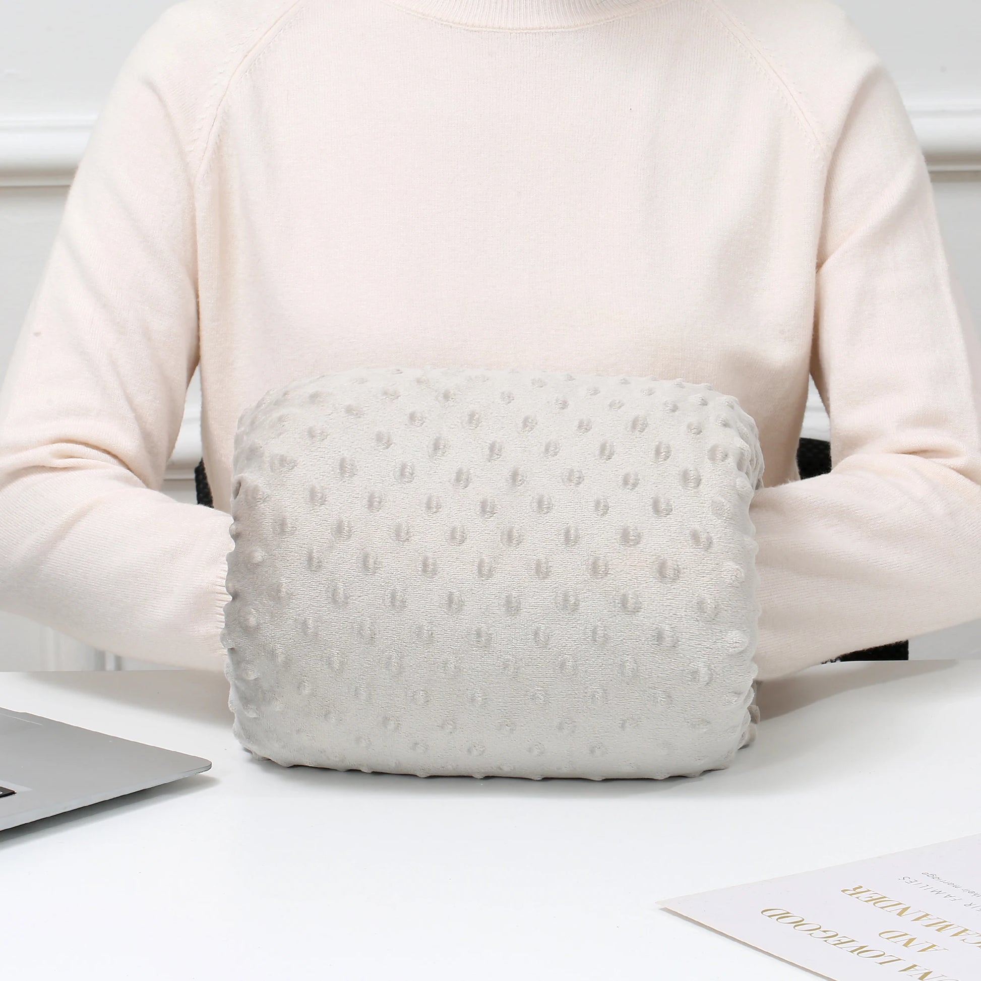 Light gray ergonomic nursing arm pillow with textured dots, worn by a person in a cream sweater.