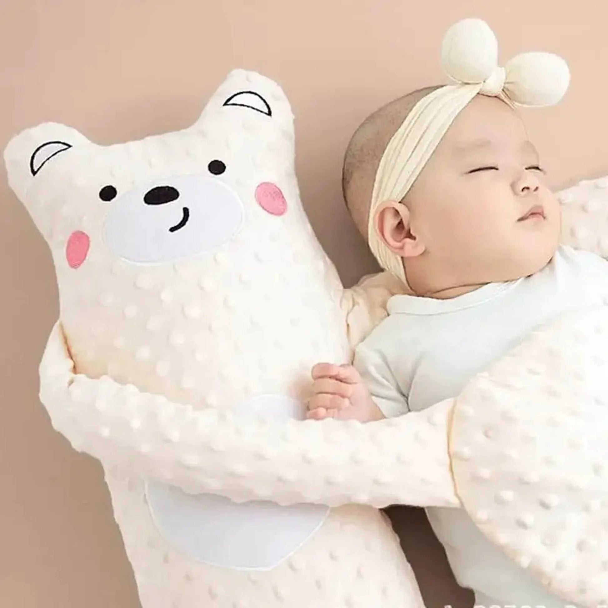 Baby sleeping soundly next to a white electric soothing pillow shaped like a bear, with soft textured fabric.