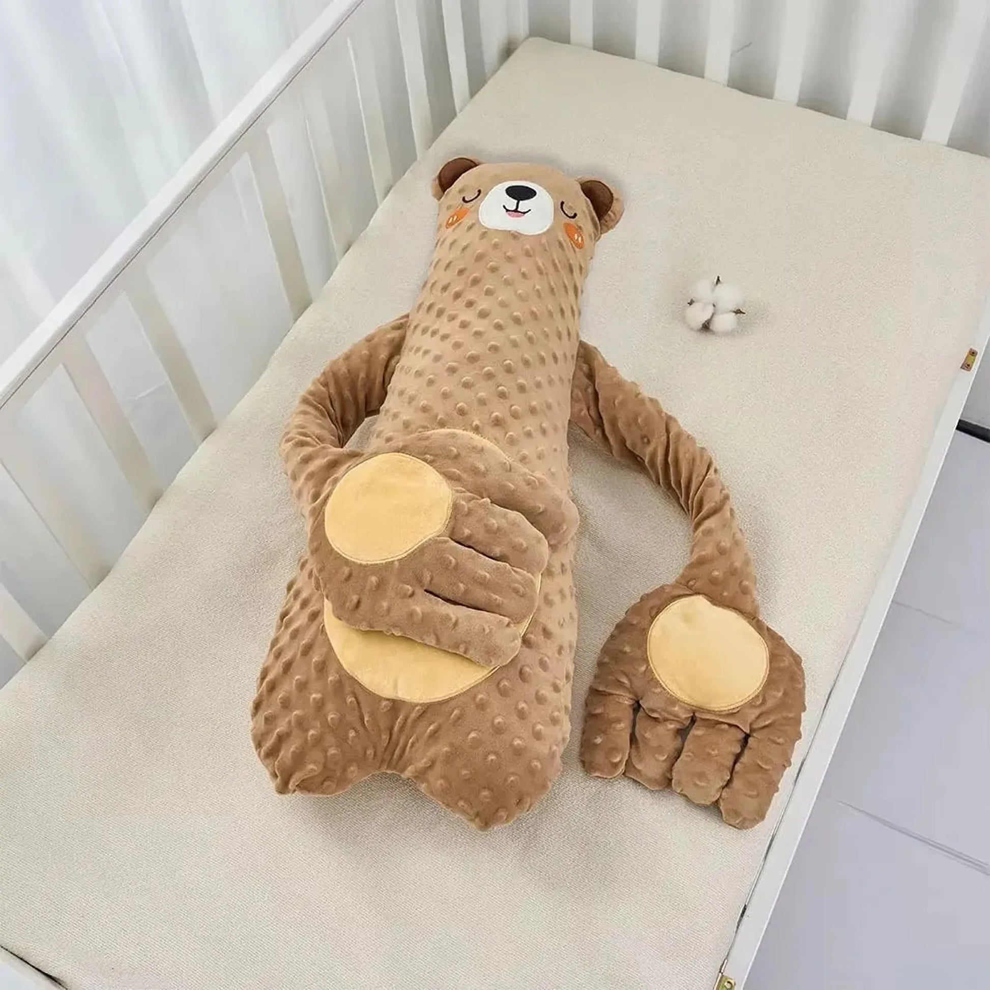 Brown bear-shaped electric soothing pillow with textured fabric and hand-like features in a crib.