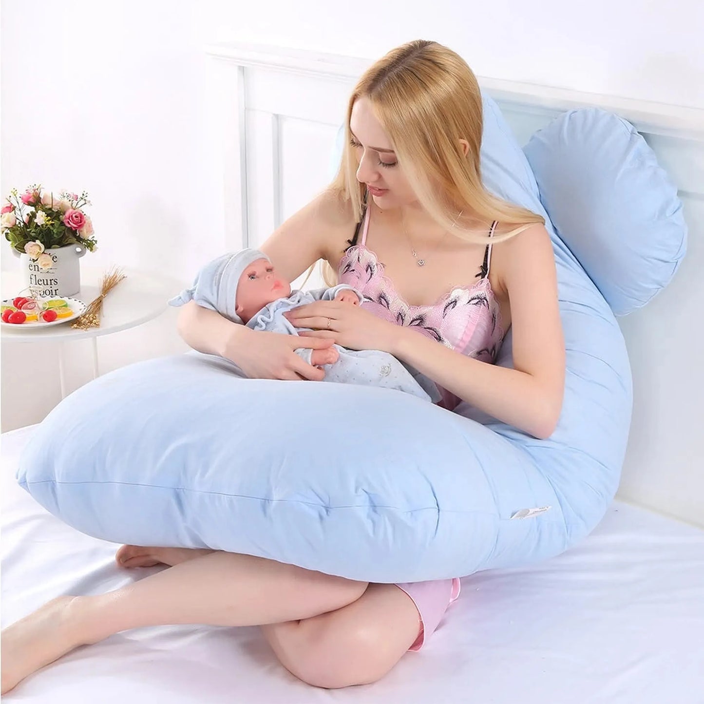 Woman holding a baby while sitting comfortably with a large light blue U-shaped full body pregnancy pillow.