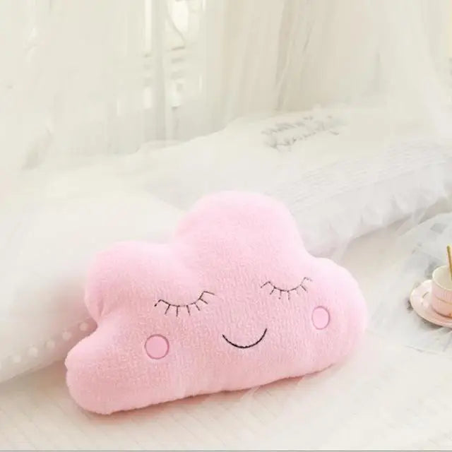 Soft pink cloud-shaped decorative pillow with embroidered sleeping eyes and a smile, for a baby's room.