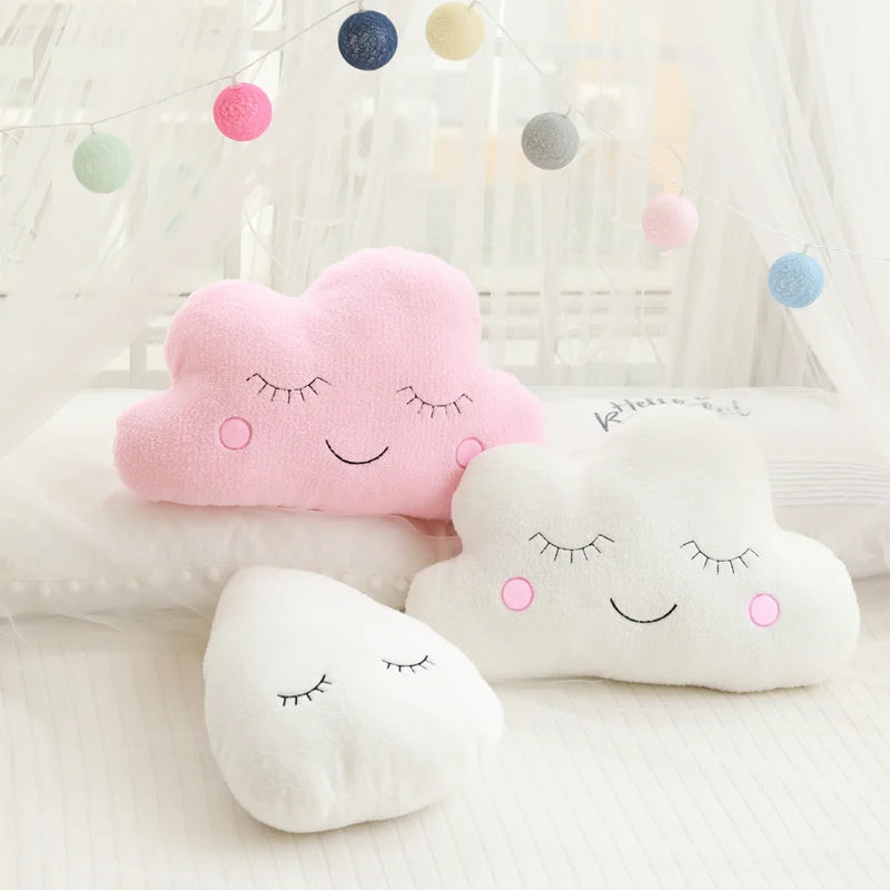 Soft pink cloud, white cloud, and white raindrop plush pillows with sleepy embroidered faces for nursery decor.