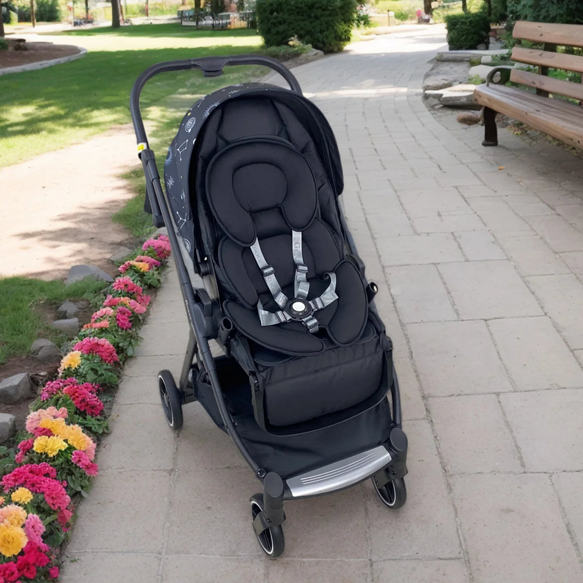 Black universal baby stroller and car seat support pillow with gray straps, in a stroller outdoors.