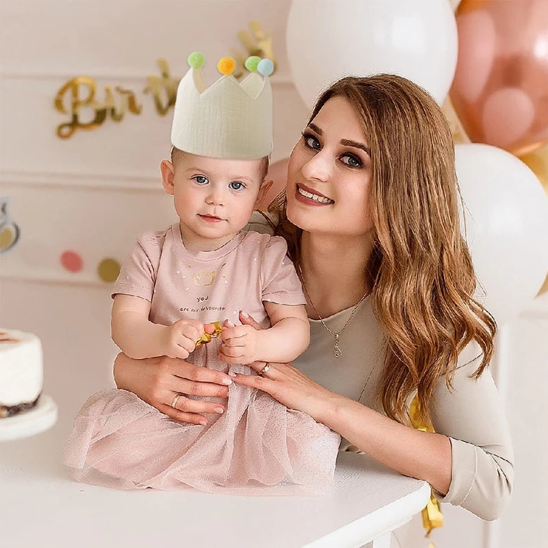 Baby's first birthday crown, cream cotton with colorful pom-poms, worn by a baby with a mother.