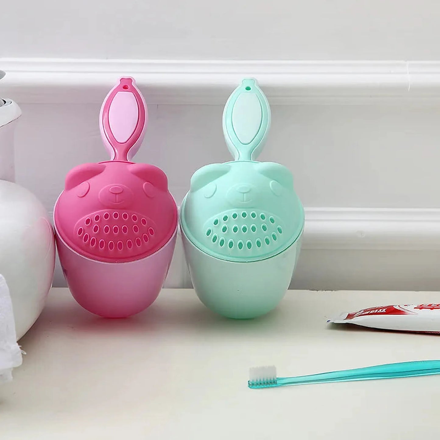 Pink and mint green bear-shaped baby bath rinse cups with comfortable handles.