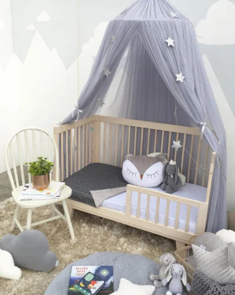 Gray tulle canopy with stars over a natural wood toddler bed, creating a dreamy nursery.