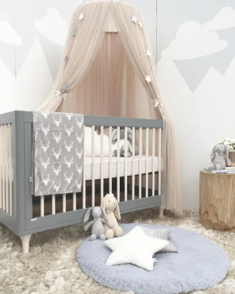 Beige tulle canopy with stars over a gray baby crib, deer blanket, and plush toys.