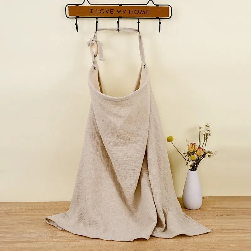 Beige cotton nursing cover and stroller blanket with adjustable strap, hanging on a wall hook.