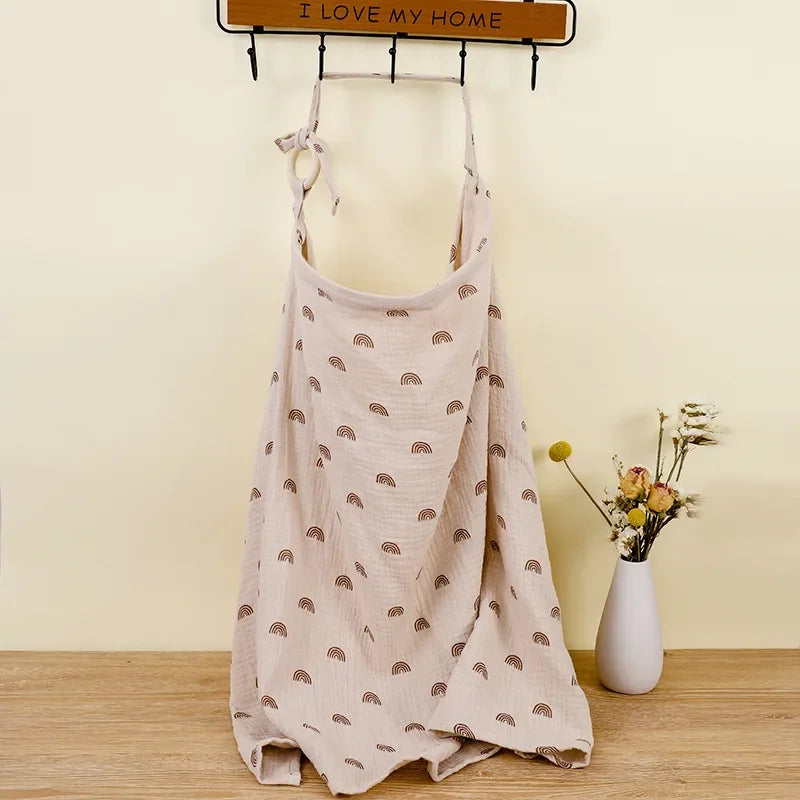 Beige cotton nursing cover with brown rainbow print, hanging on a hook.