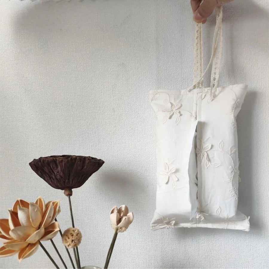 White French lace tissue box cover with floral embroidery, held by hand, next to dried flowers.