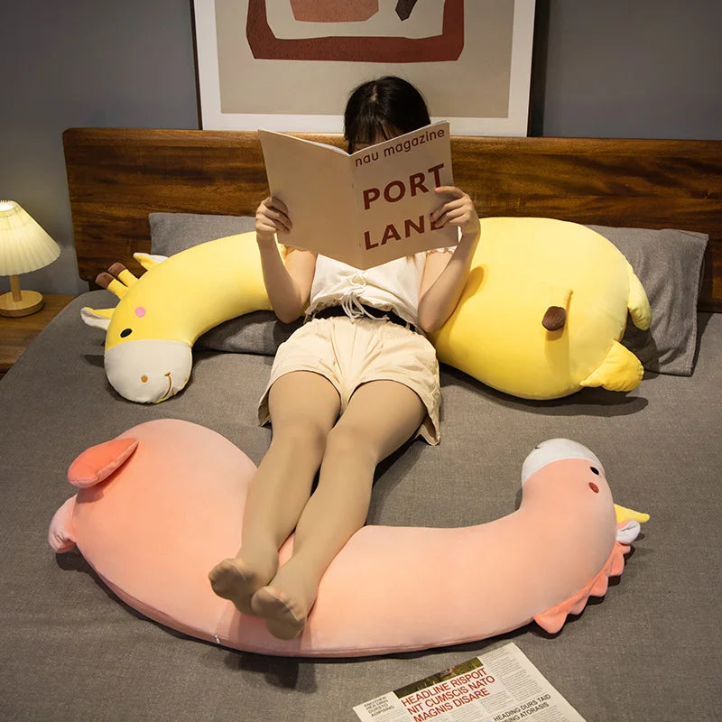 Soft pink flamingo and yellow giraffe plush pillows on a bed with a person reading.