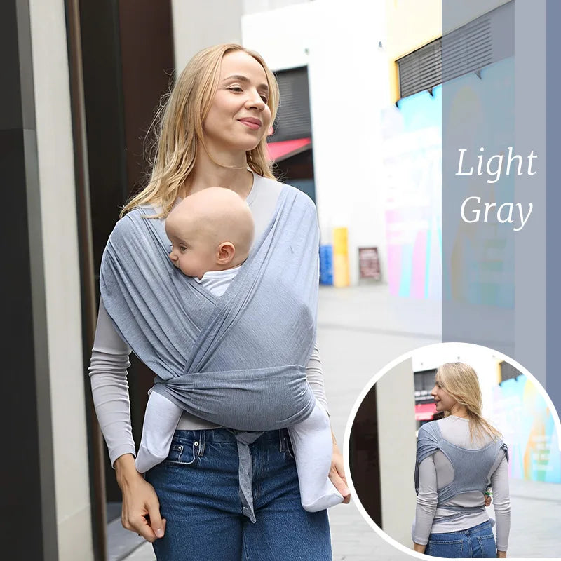 Woman wearing a light gray ergonomic cotton baby wrap carrier with a baby facing inward.