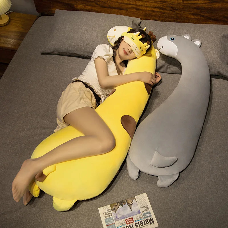 Soft yellow giraffe plush pillow and gray hippo plush pillow on a bed with a woman.