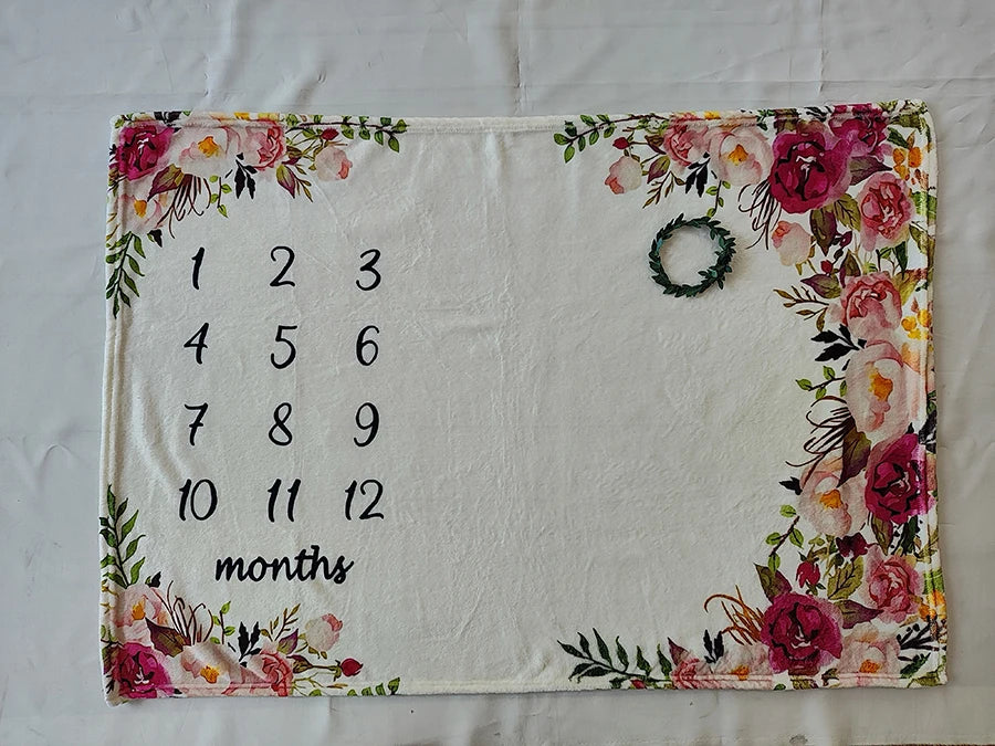 Soft white polyester baby milestone blanket with pink floral border and numbers 1-12, includes a green wreath prop.