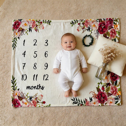 Baby on a white floral milestone blanket with numbers 1-12, a pillow, and dried flowers.