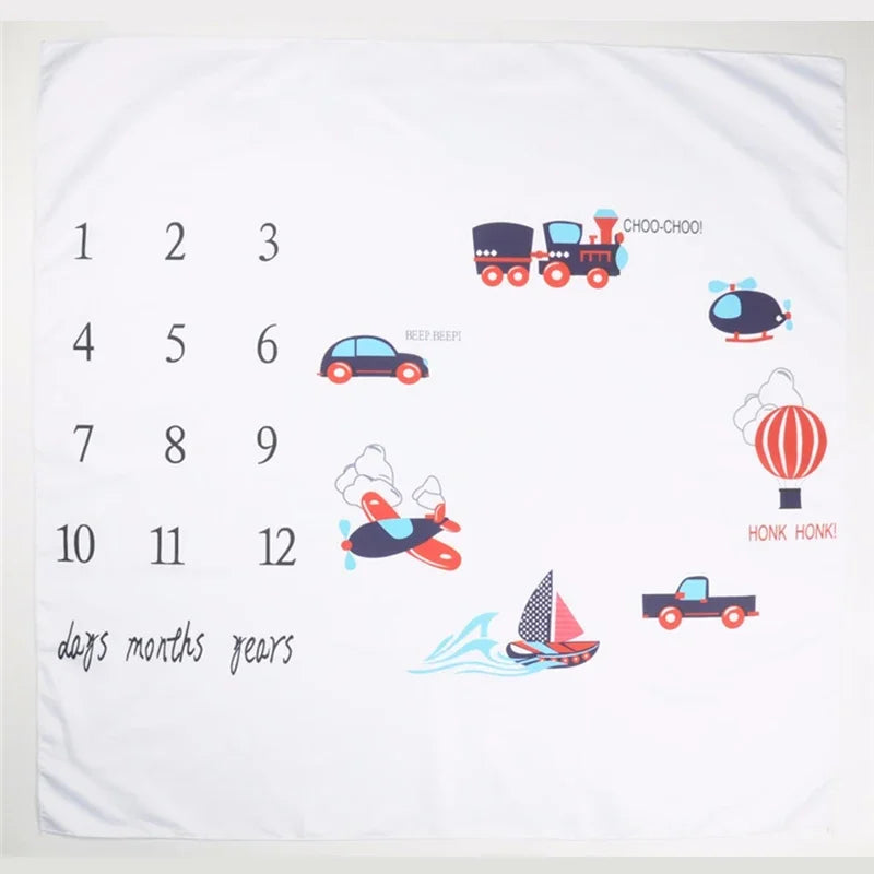 White polyester baby milestone blanket with numbers 1-12 and colorful transportation vehicle illustrations.