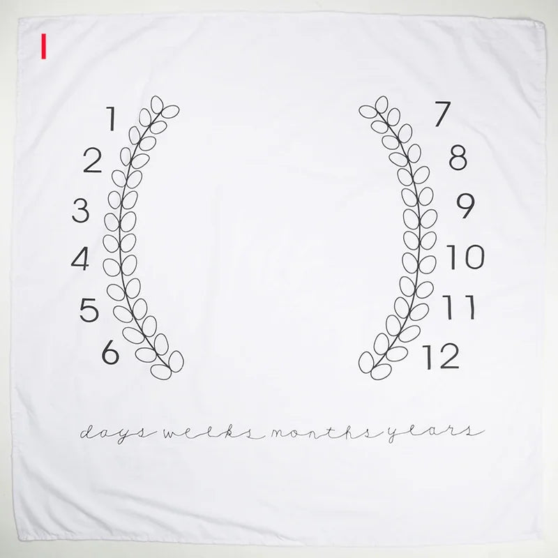 White polyester baby milestone blanket with black numbers 1-12 and leaf wreaths for monthly photos.