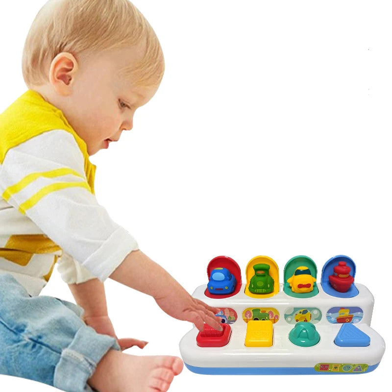 Toddler playing with a colorful interactive pop-up toy featuring vehicles and shape buttons.
