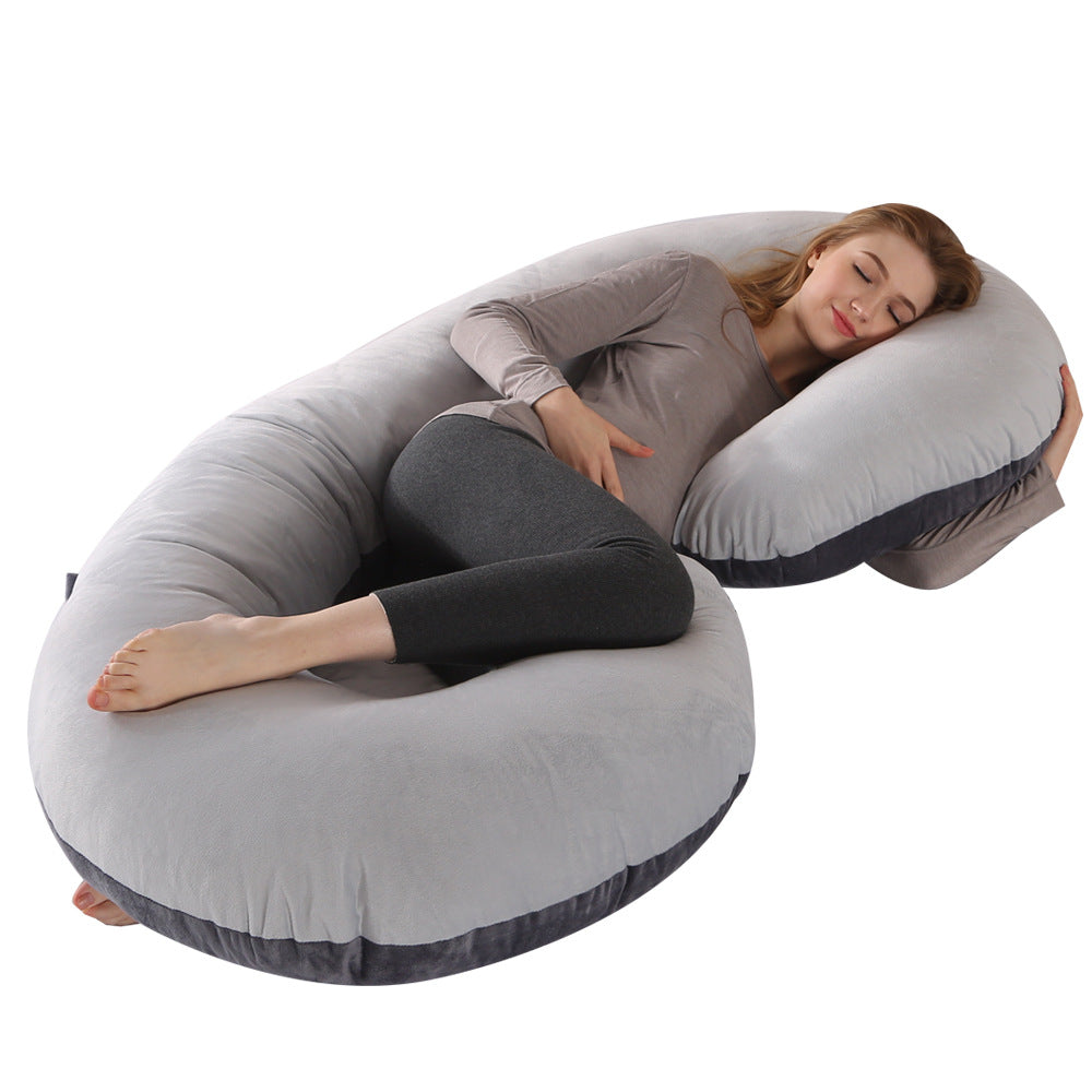 Pregnant woman sleeping soundly on a large, soft gray C-shaped velvet pregnancy pillow with dark gray trim.