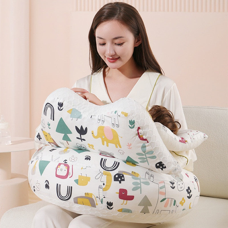 Woman breastfeeding baby using a white, multi-functional nursing pillow with colorful animal and nature patterns.