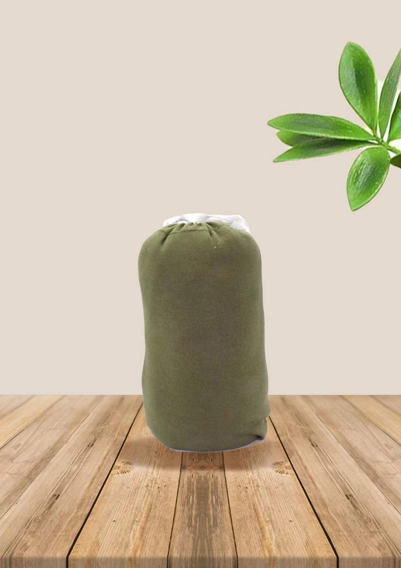 Rolled up olive green soft cotton ergonomic baby wrap carrier on a wooden surface with green leaves.