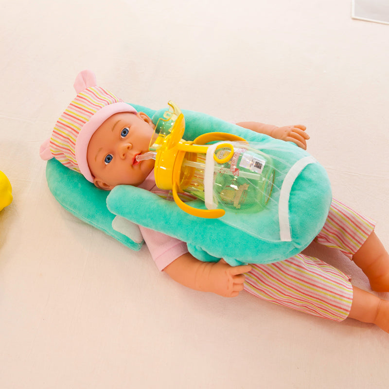 Plush teal baby feeding pillow supporting a doll with a bottle, featuring a soft velvet cover and ergonomic design.