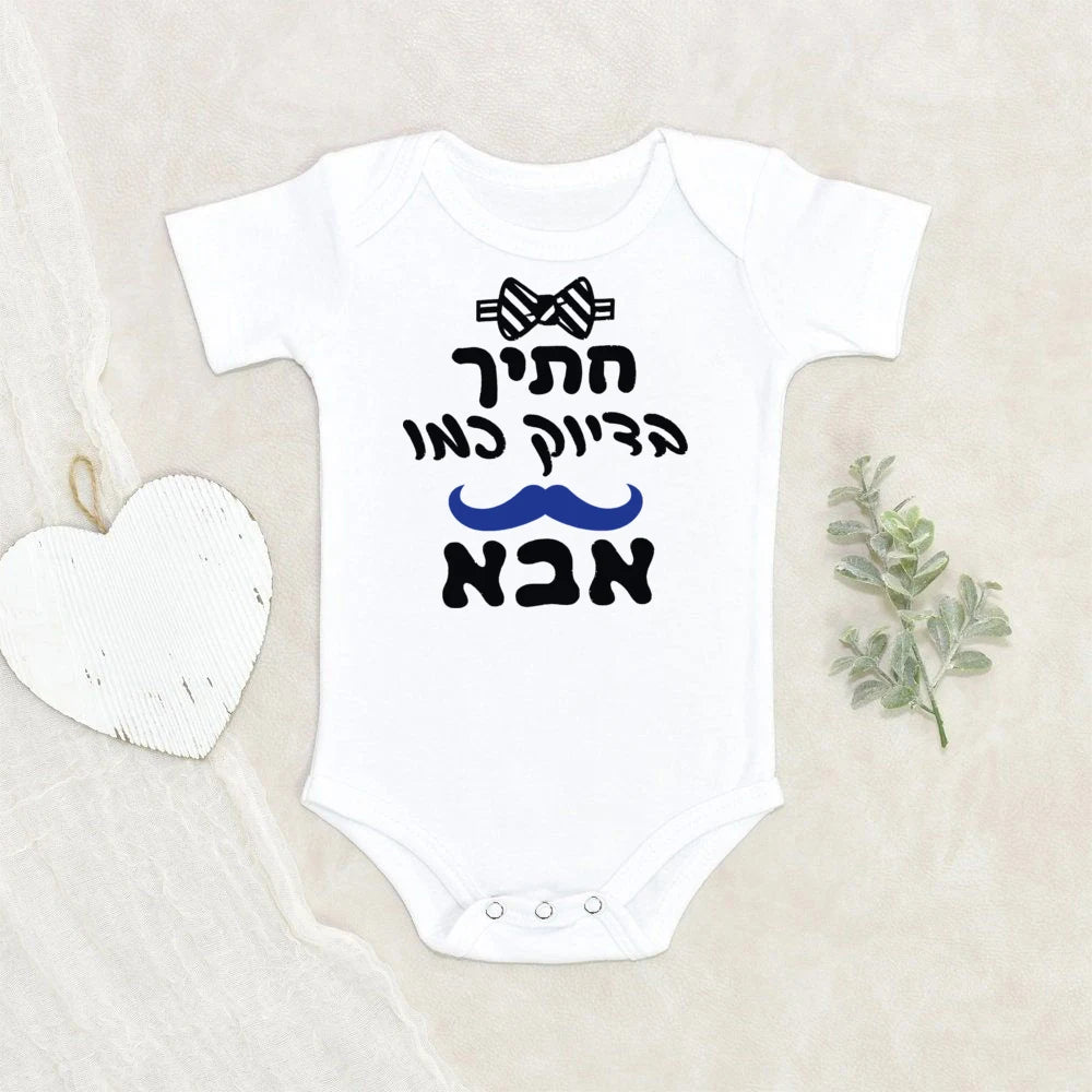 White baby bodysuit with "Handsome like Dad" Hebrew text, bow tie, and blue mustache graphic.