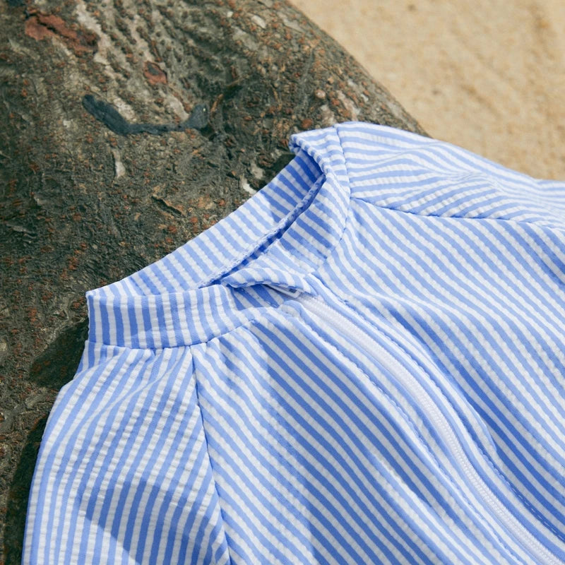 Blue and white striped short-sleeve baby swimsuit with a half-zip, made of polyester and elastane.