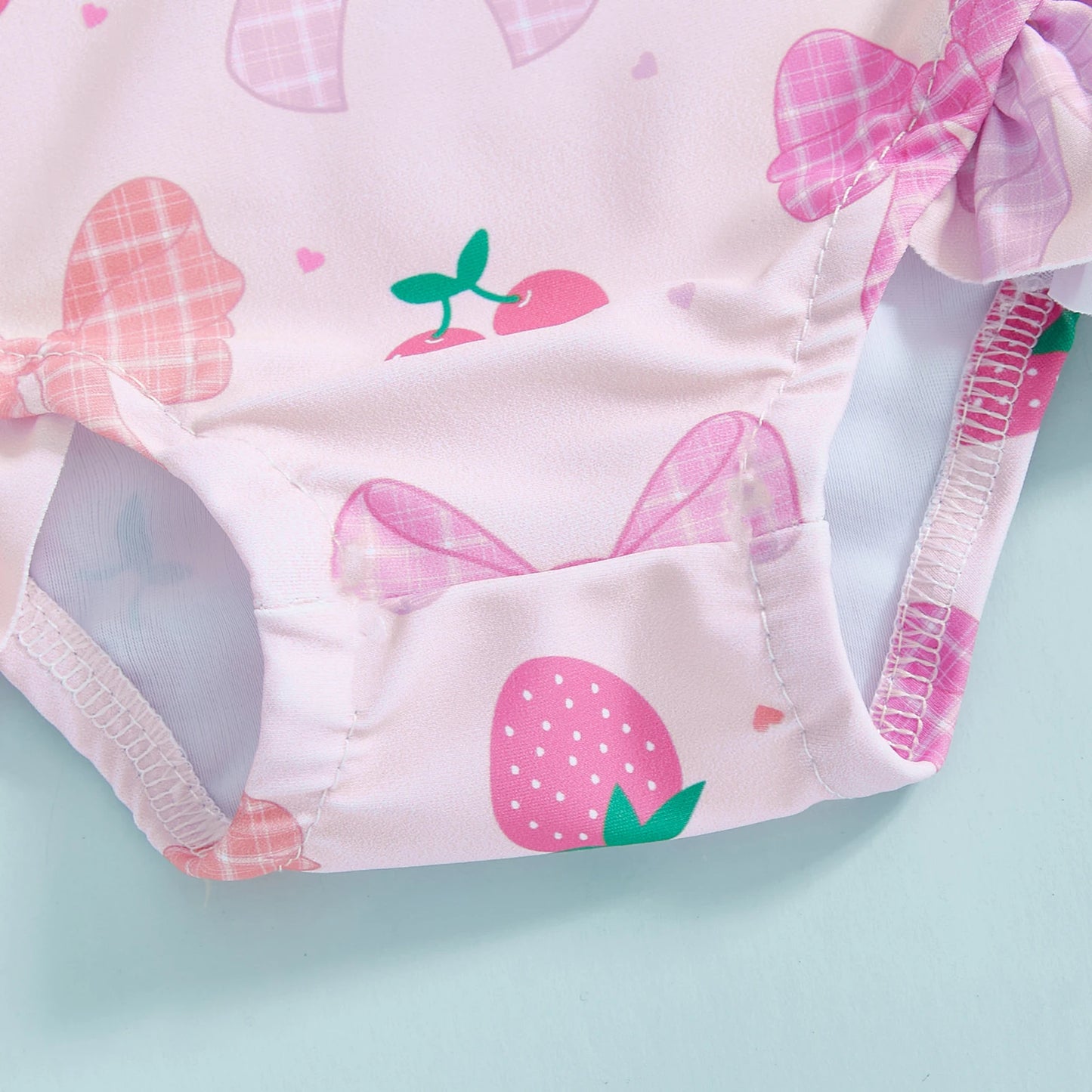 Pink long-sleeve rashguard swimsuit for babies with strawberry and bow print, 100% polyester.