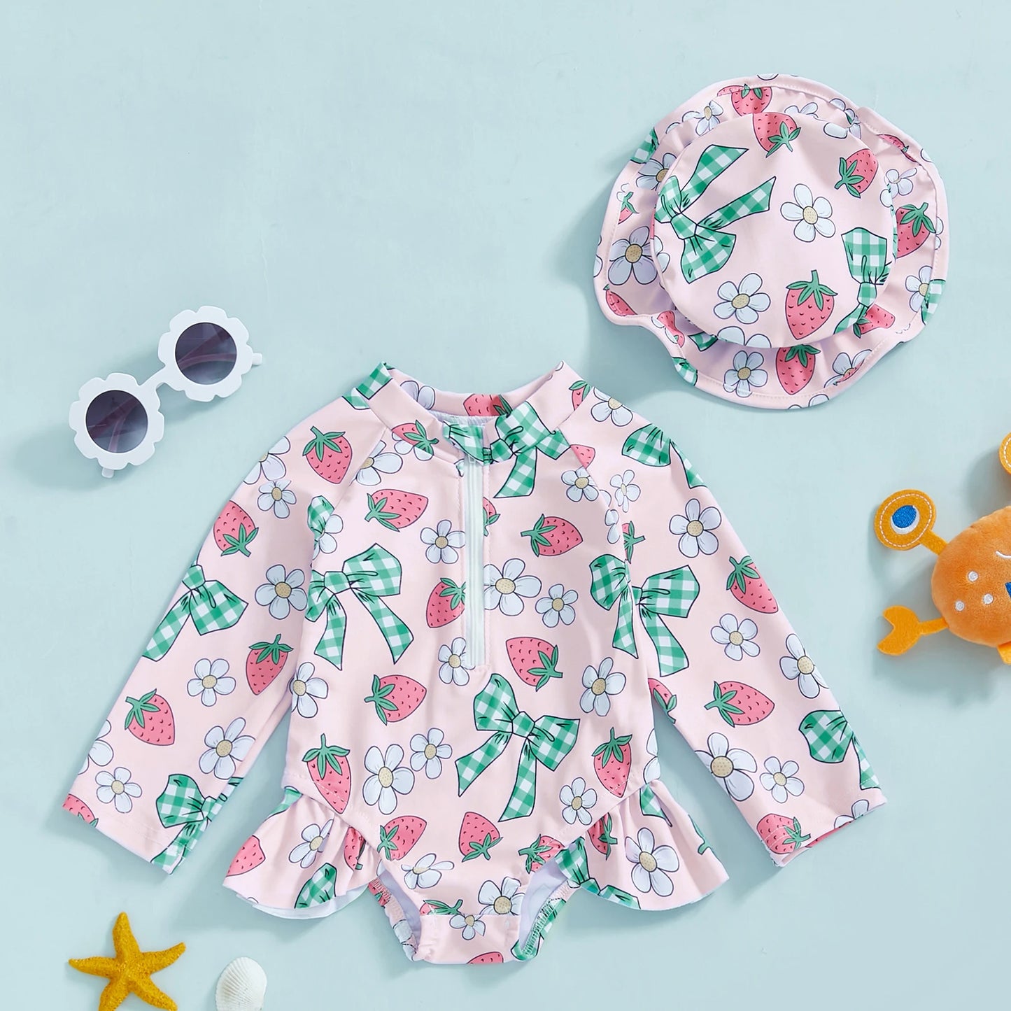 Pink long-sleeve rashguard swimsuit for babies with strawberry and bow print, matching sun hat.