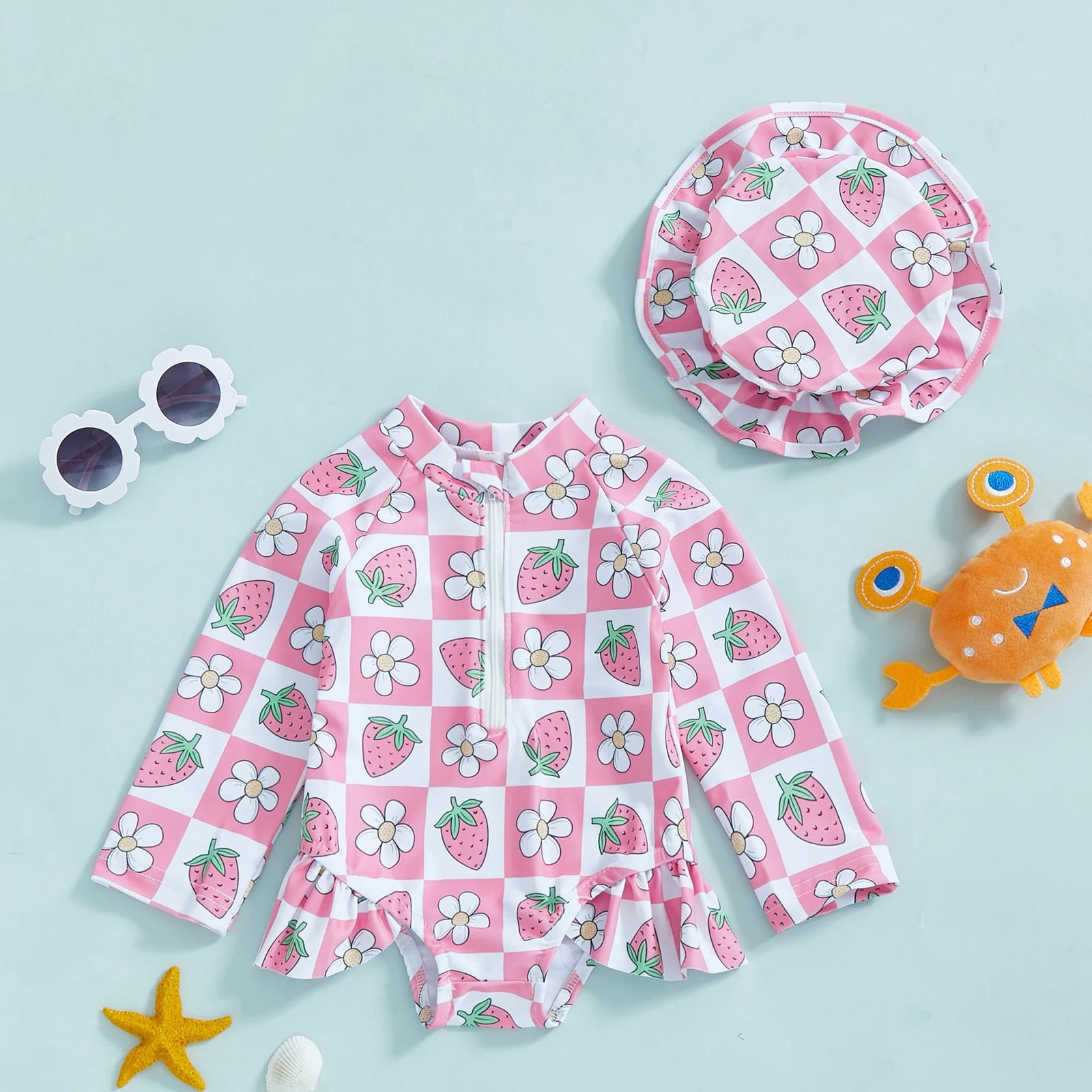 Pink and white checkered long-sleeve rashguard swimsuit for babies with strawberry and flower print, includes matching hat.