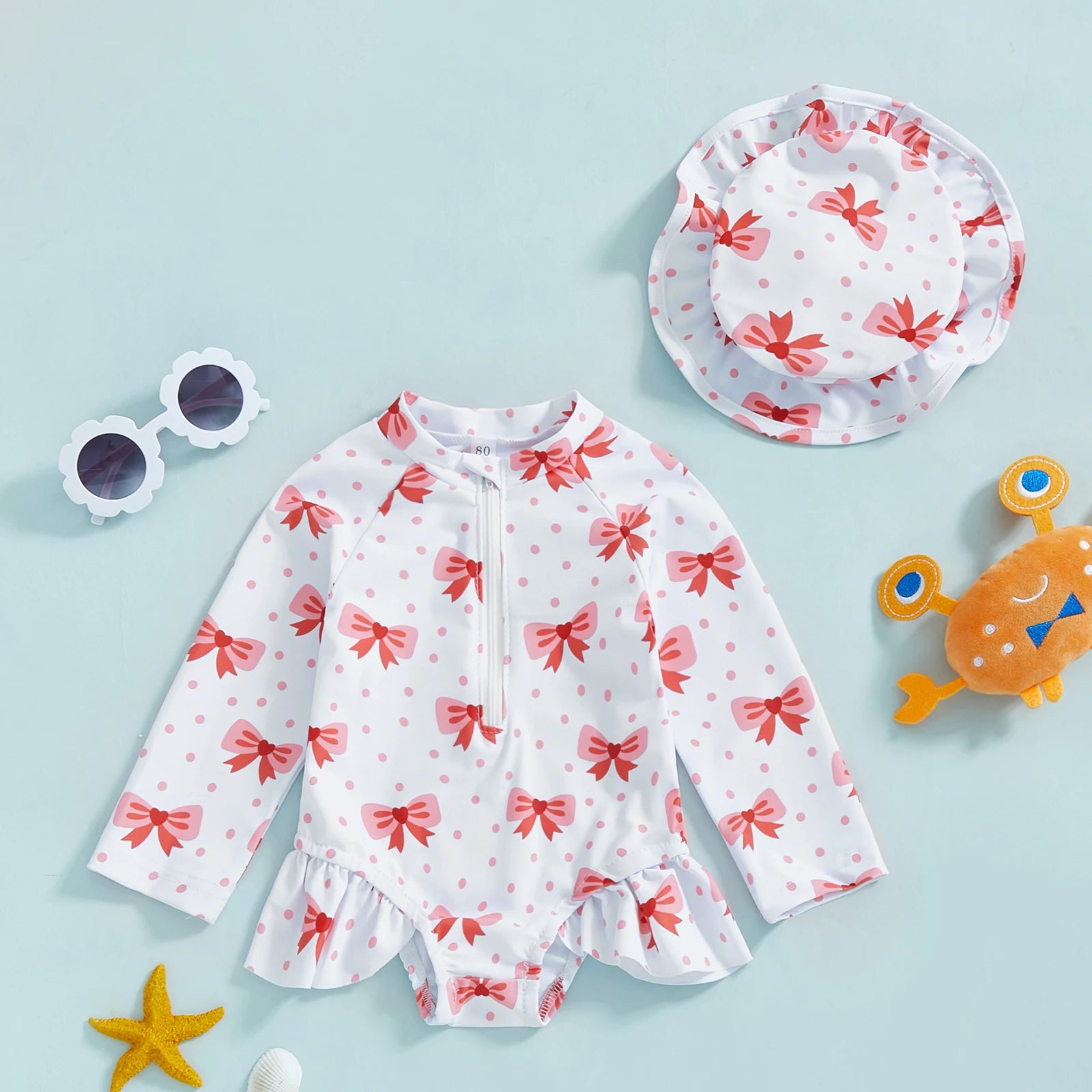 White long-sleeve rashguard swimsuit for babies with pink bows, matching sun hat, and zipper.