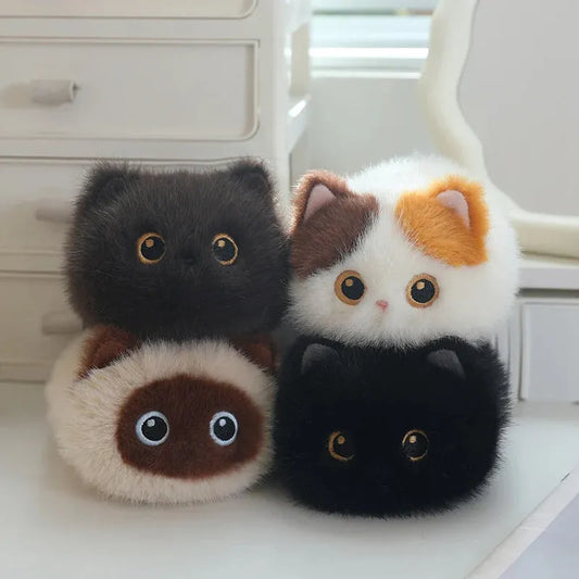 Four soft, round plush cat toys in black, white/brown/orange, cream/brown, and black, with big eyes.