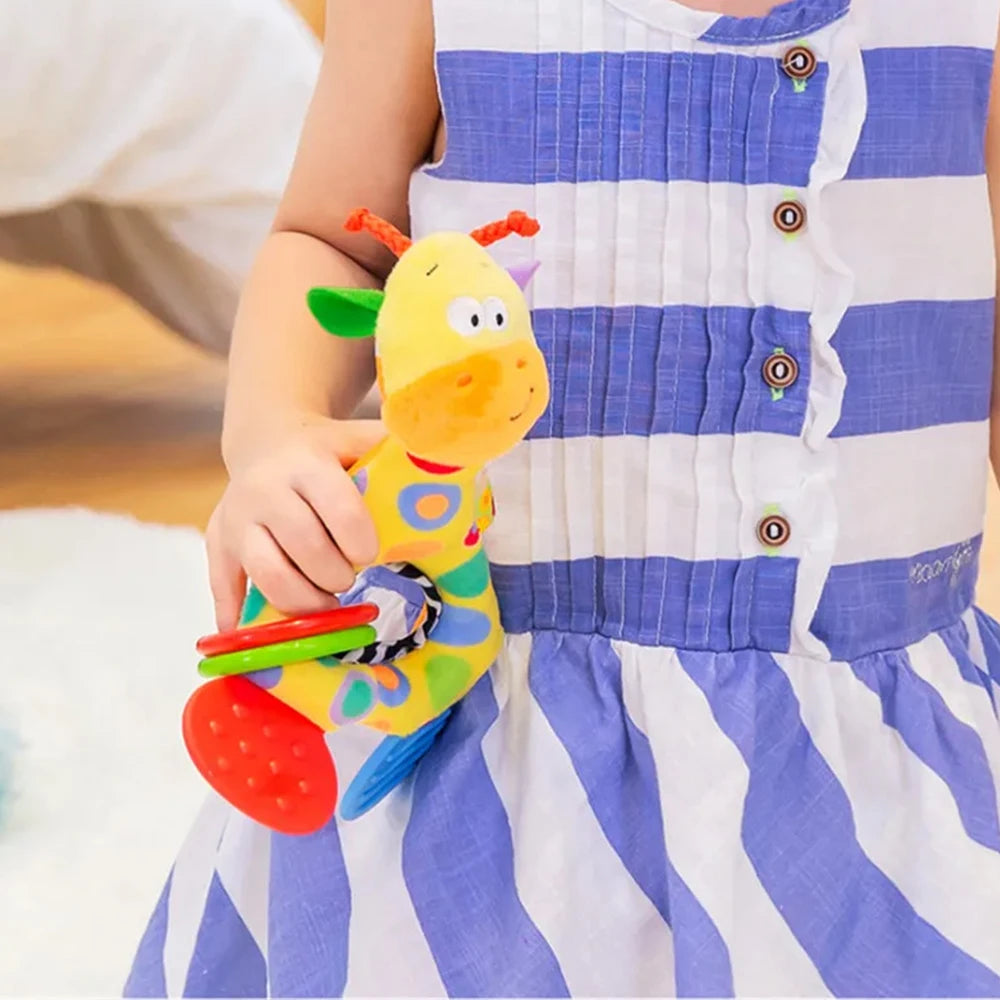 Soft plush giraffe baby teether rattle with colorful rings, held by a child in a striped dress.