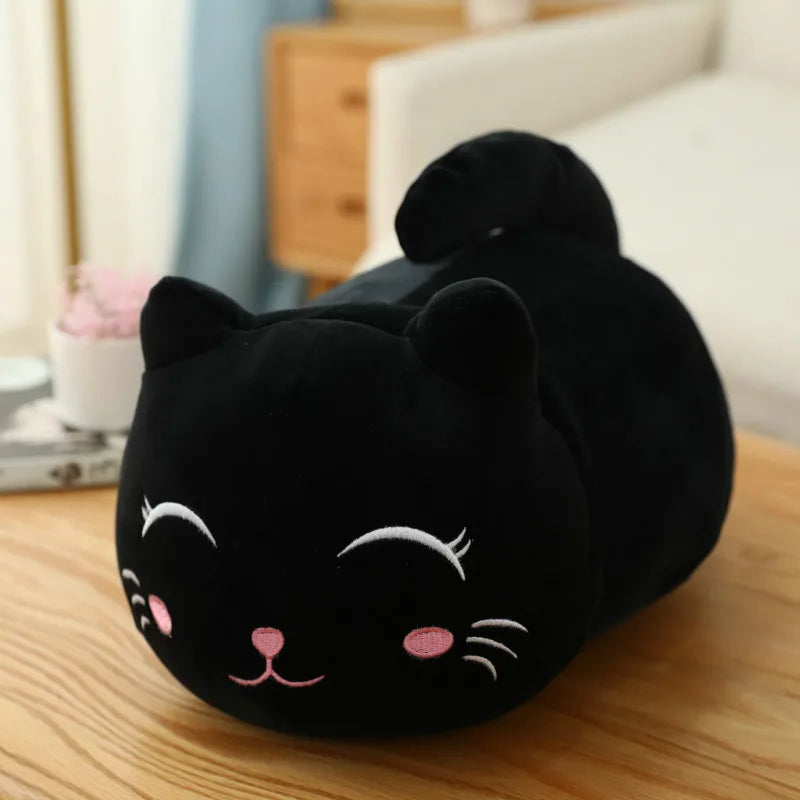 Soft black plush cat toy with pink cheeks and white embroidered eyes, lying on a wooden table.