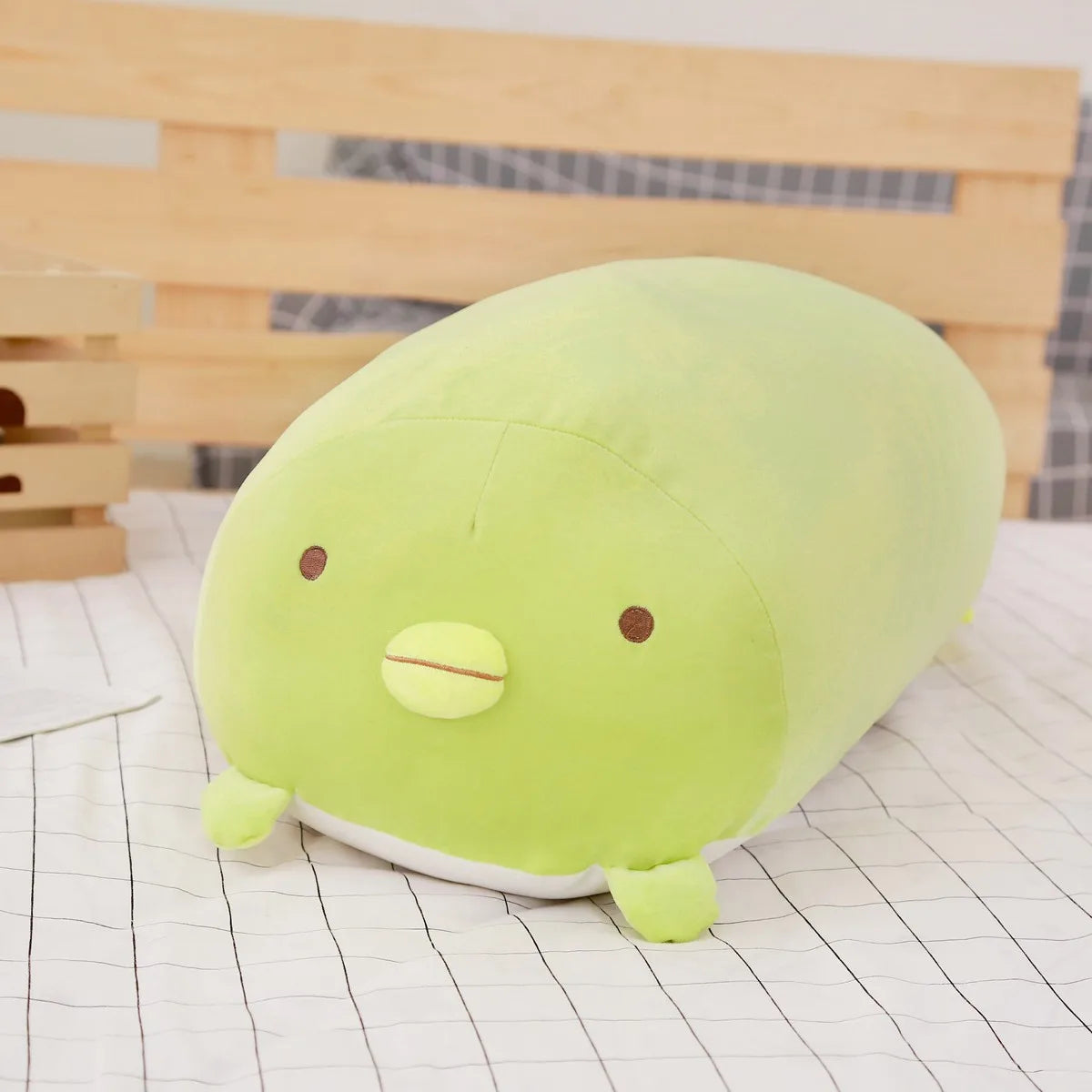 Soft green plush animal pillow with brown eyes and yellow beak, on a checkered bed.