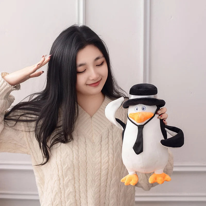 Soft 28cm Madagascar penguin plush toy with black hat and tie, held by a woman.