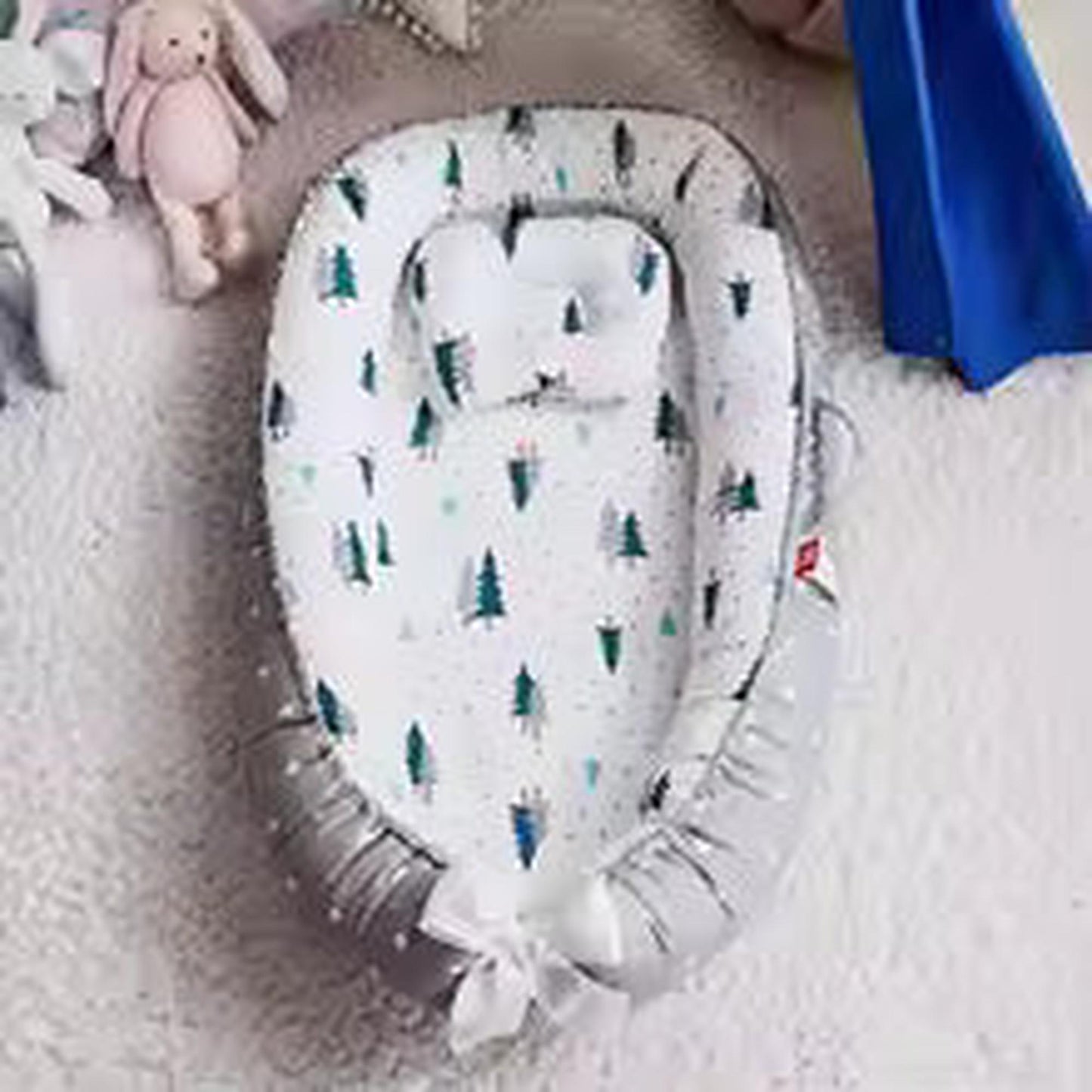 Adjustable white baby nest with green tree print, grey sides, and a bow.