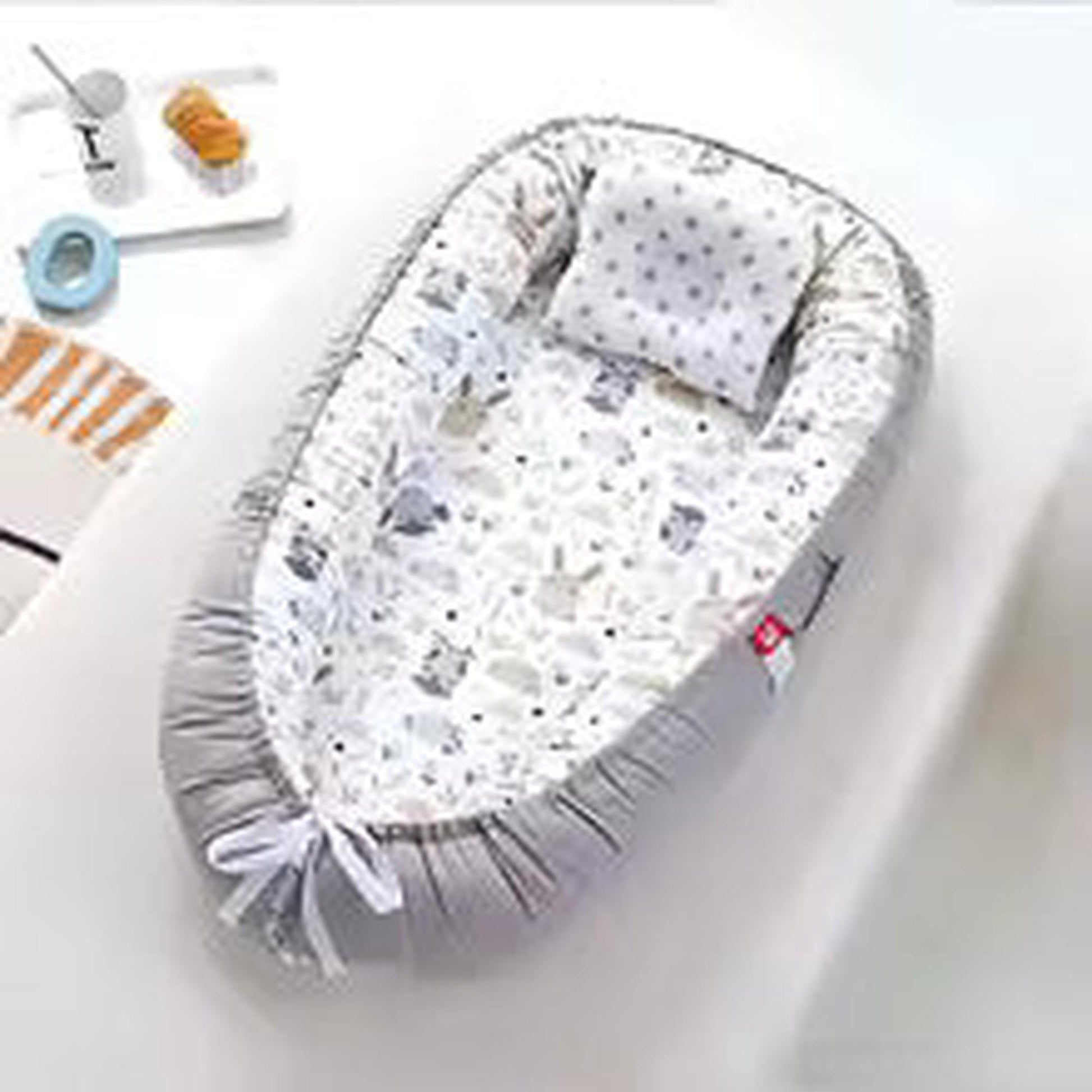 Adjustable grey baby nest with white animal print and polka dot pillow.