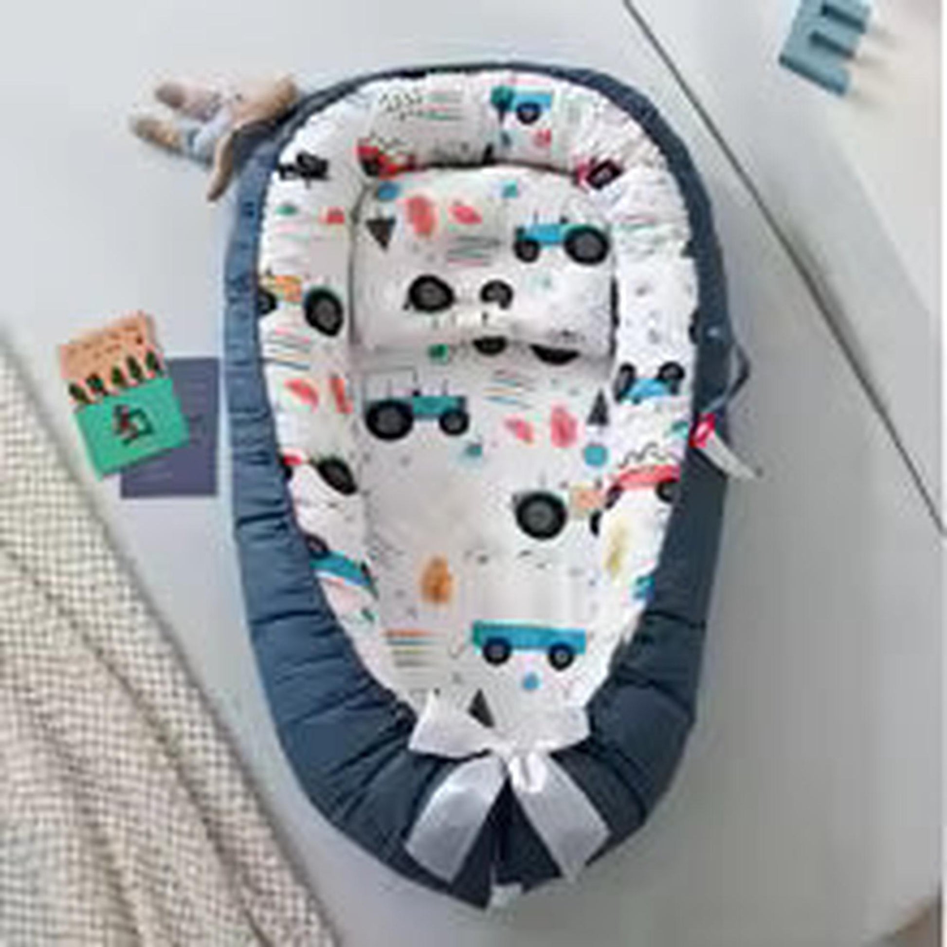 Adjustable baby nest in blue with a white cotton insert featuring colorful vehicle patterns.