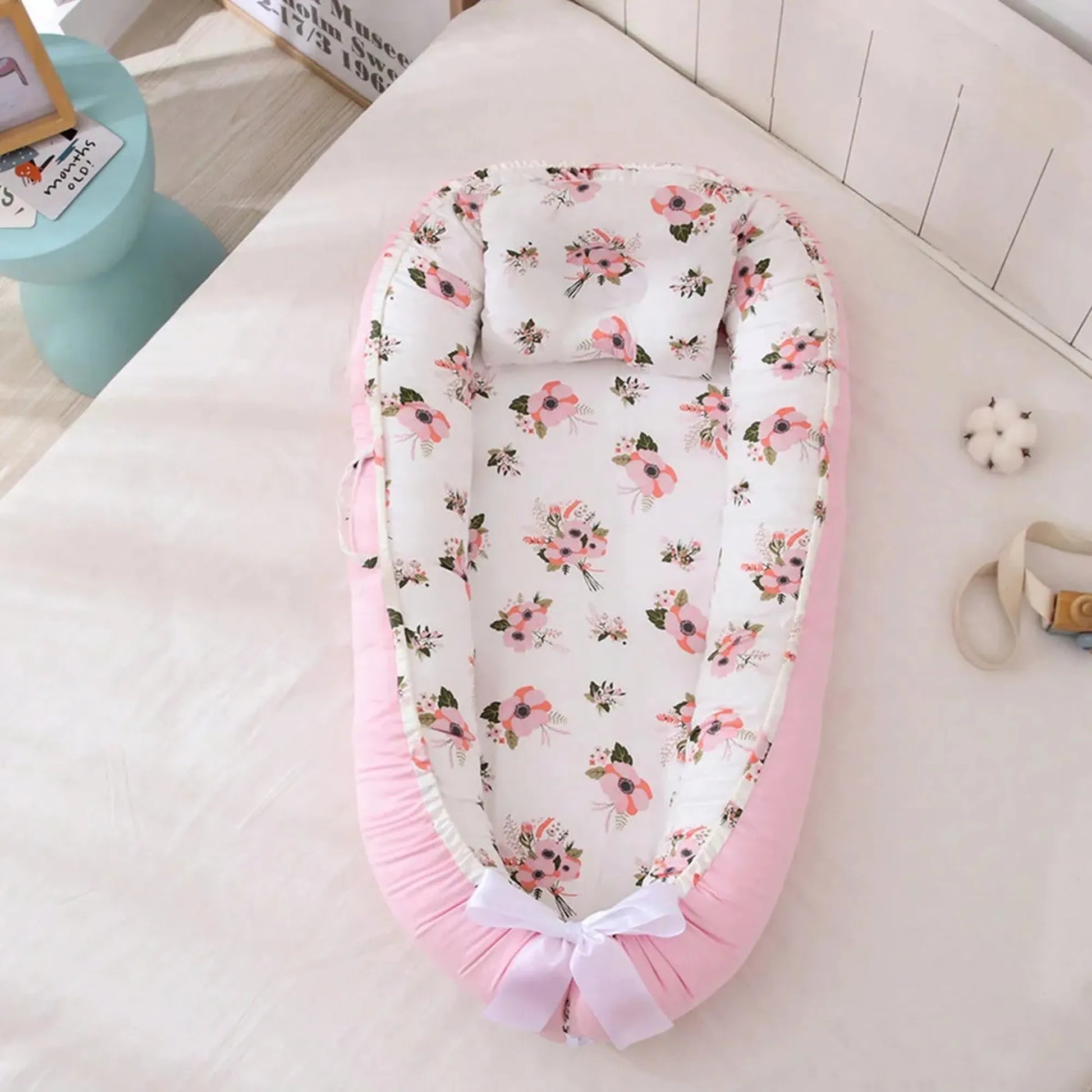 Pink baby nest with white floral print interior, adjustable drawstring, and white bow.
