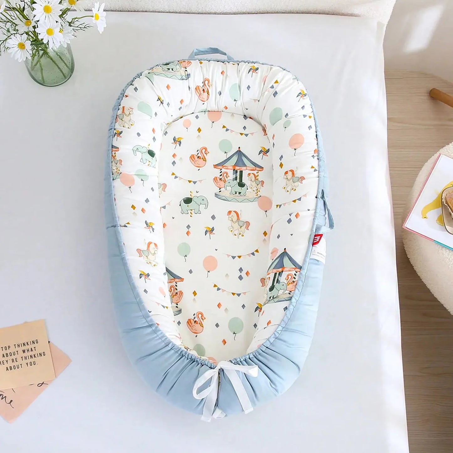 Adjustable baby nest in light blue with a colorful carousel and animal print.