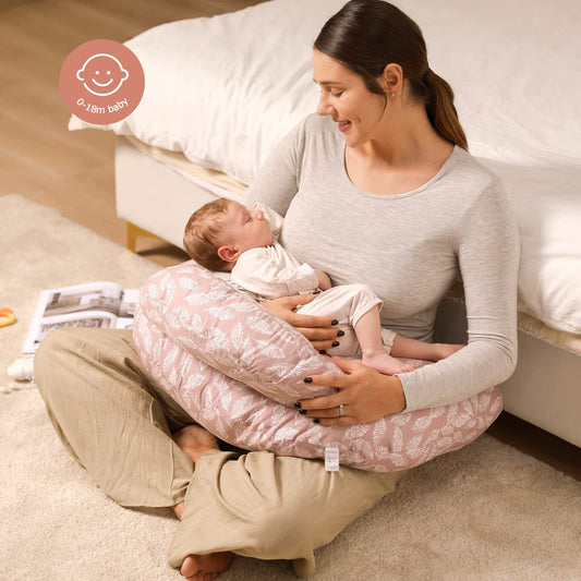 Mother holding a sleeping baby on a pink nursing pillow with a white leaf pattern.