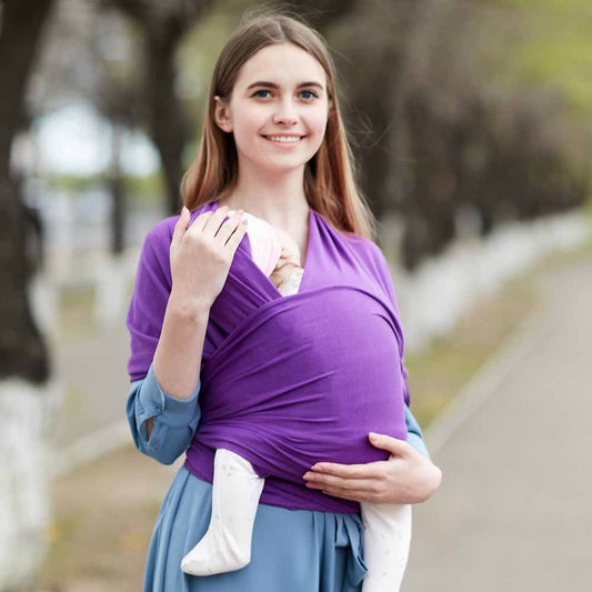 Smiling woman wearing a soft purple cotton baby wrap carrier with a sleeping infant.